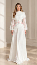 Front view of woman wearing white draped high neck long sleeve maxi dress with floral appliqué